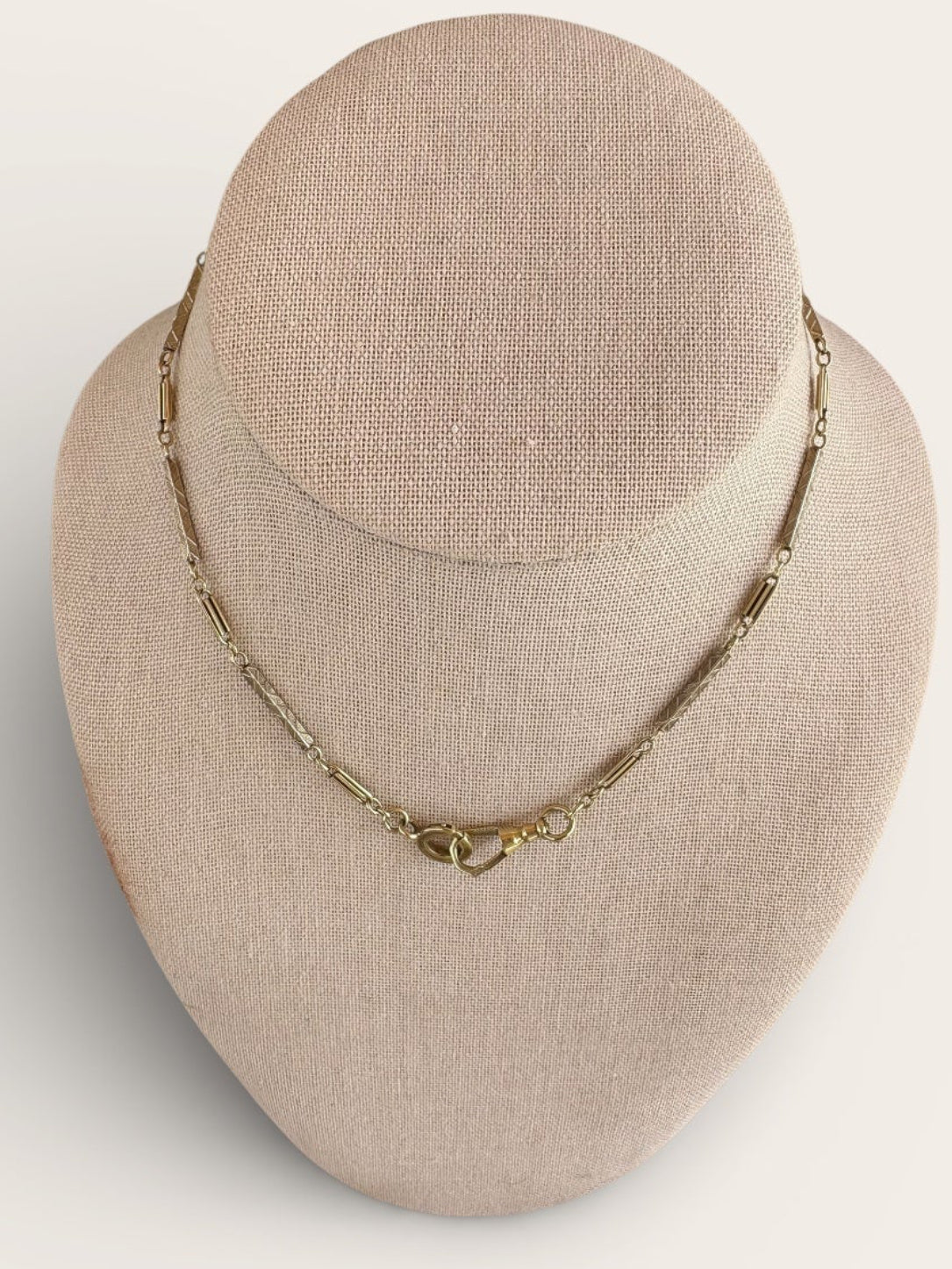Gold necklace on a beige bust against a white background